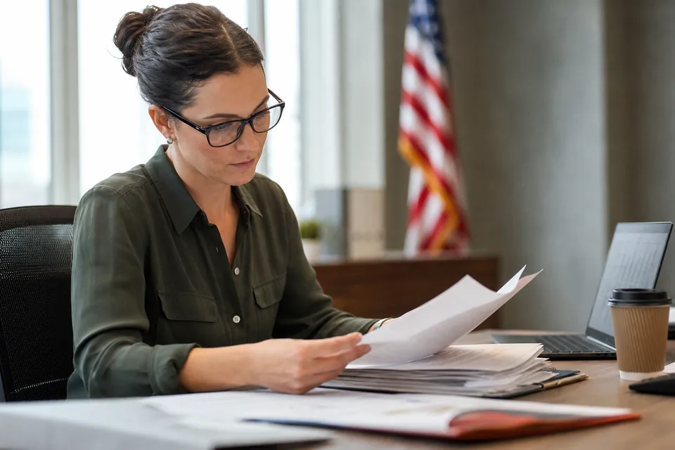 Public sector lease accountant reviewing printed property leases next to a laptop spreadsheet