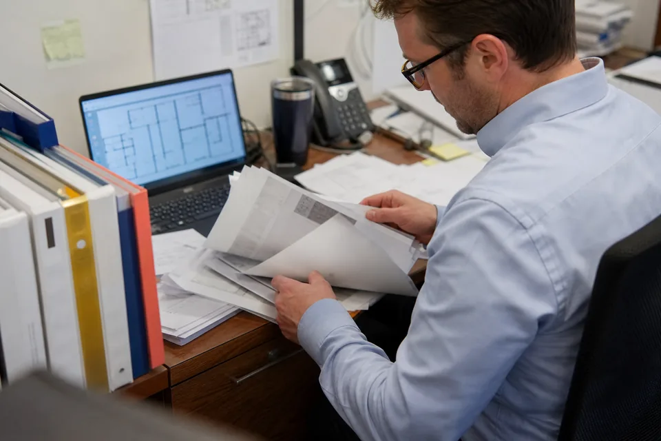Real estate manager reviewing printed commercial leases next to a laptop with a floor plan